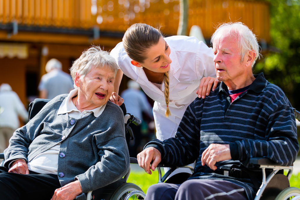 Old couple, senior man and woman, in garden of retirement home with nurse